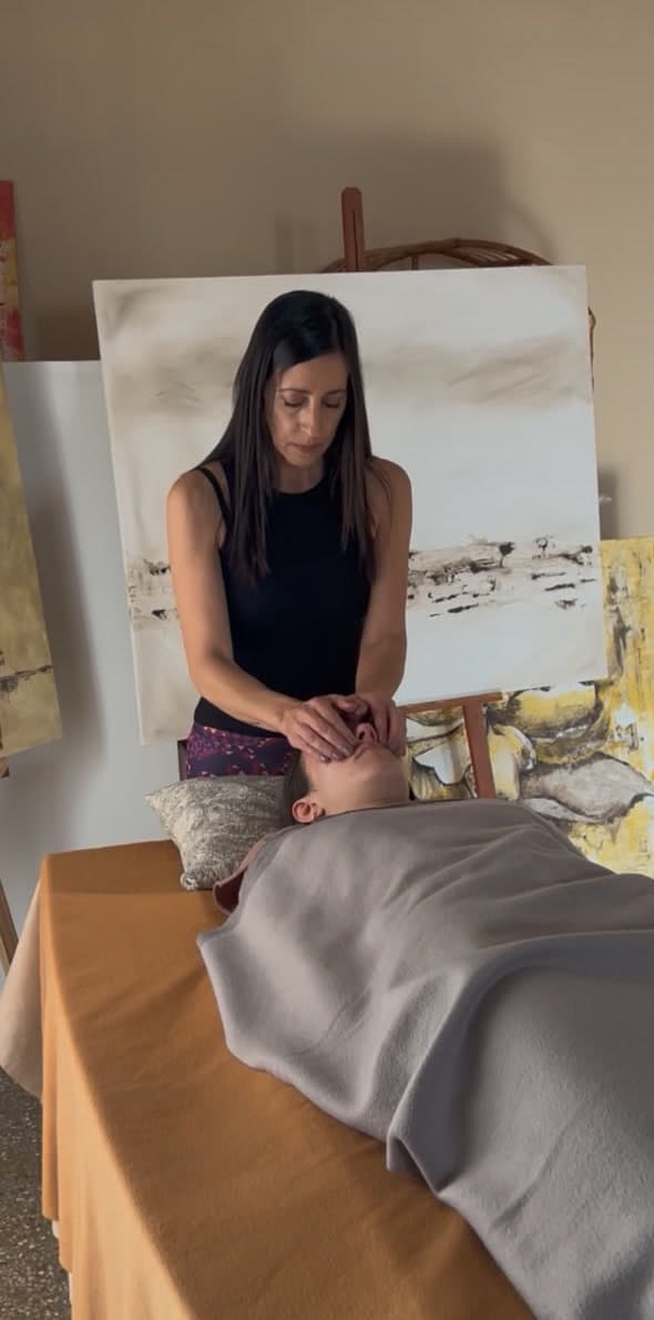 Andrea apoya las manos sobre el rostro de una persona recostada durante una sesión de reiki
